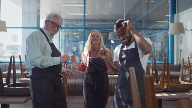 Multiethnic restaurant owners smile and dance in empty cafe. Realtime