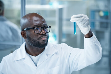 Serious African doctor in eyeglasses testing samples in flask during scientific exam in laboratory