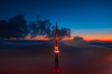 Obraz premium Glowing TV tower in the fog at sunset. Filmed on a drone.
