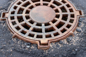 Cast-iron stormwater drainage hatch on the road before asphalt pavement. Drainage of rainwater from the road surface. Close-up.