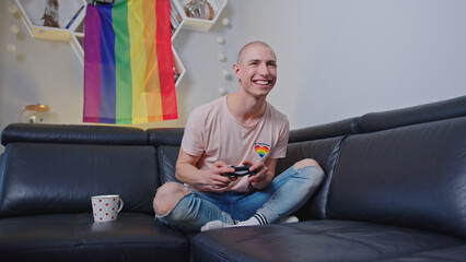 Happy queer non-binary person playing video games in their free time while sitting on a black sofa...
