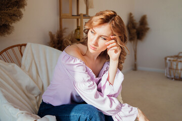 Obraz premium Portrait of a fashionable young woman sitting in a wicker chair in the sun in a room.