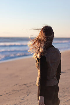 Backview of young woman by sea. Flying hair in windy day. Vertical photo. Banner, copy paste and text space.
