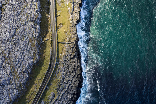 Top down view on a small road by a rough stone coastline. Rock formation and ocean water surface. Burren, Ireland