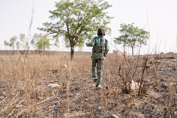 Rear view of a little black African boy walking in the midst of scrub in a dry cornfield in the...