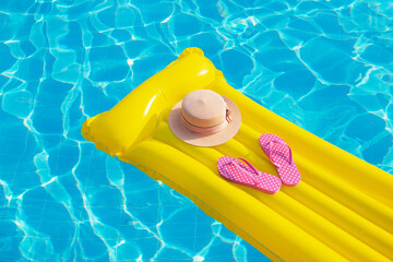 Beach summer holiday background. Inflatable air mattress, flip flops and hat on swimming pool.