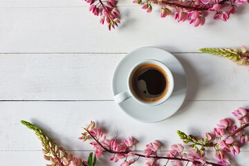 coffee cup with saucer and pink lupine flowers on board white wooden background. Place for your...