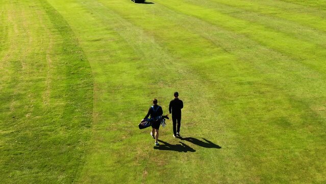 Back view of golfer and caddie walking on green field, Hills Golf Club in Molndal near Gothenburg, Sweden. Aerial forward
