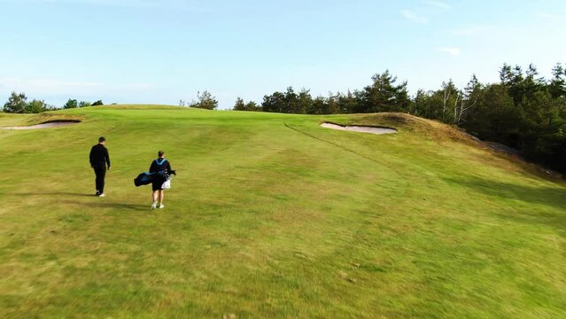 Back view of golfers walking on slope of Hills Golf Club in Molndal near Gothenburg, Sweden. Aerial forward