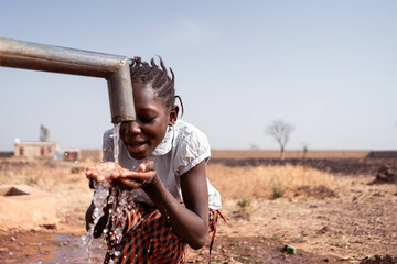 Clean water supply concept: young black African native girl drinking healthy fresh water from a...