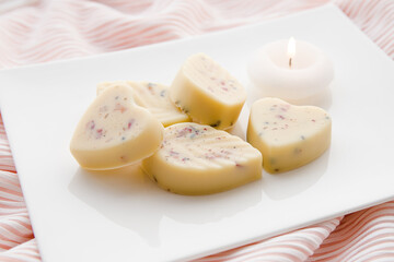 Small heart and leaf shape bath truffles, buttery version of the bath bomb in bathroom on white tray with candle burning. Home spa concept.