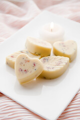 Small heart and leaf shape bath truffles, buttery version of the bath bomb in bathroom on white tray with candle burning. Home spa concept.