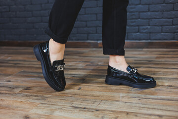 Close-up female legs in black trousers and leather black shoes. Women's shoes in patent leather with a metal buckle. New spring-summer collection of women's leather shoes 2022