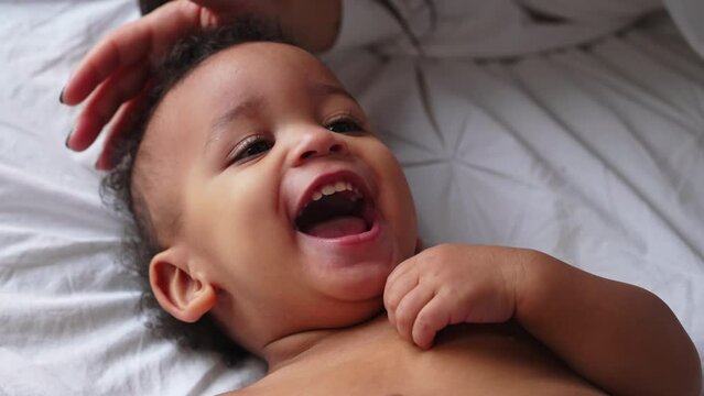 Amused biracial toddler smiling and laughing with his parents while laying down on the bed. High quality 4k footage