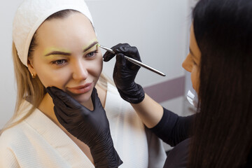 The hand of a make-up artist in black gloves applies a yellow eyebrow paste to the eyebrow....
