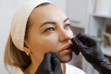 Young woman with permanent makeup on her lips in a cosmetologists salon. Permanent makeup tattoo....