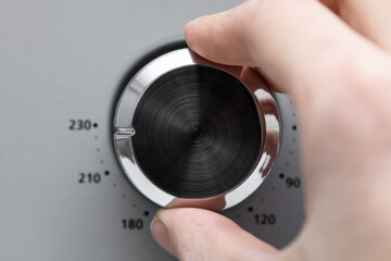 Hand twists round temperature adjustment button in the microwave oven. Button to warm food on gray background