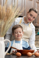 A young beautiful mother with her son at home in the kitchen prepare dough for baking cookies against the background of ears of wheat. On the table are eggs and a rolling pin. selective focus