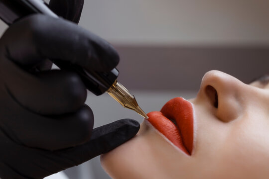 Cosmetologist makes permanent makeup on a woman's face. Specialist applies a tattoo on the patient's lips close-up