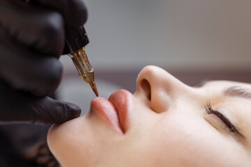 Cosmetologist makes permanent makeup on a woman's face. Specialist applies a tattoo on the patient's lips close-up