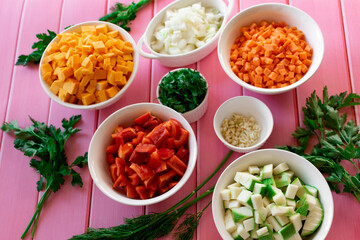 Different diced fresh vegetables and greens, fruits of different color and taste, on a pink wooden table, preparation for cooking in the kitchen, colorful ingredients
