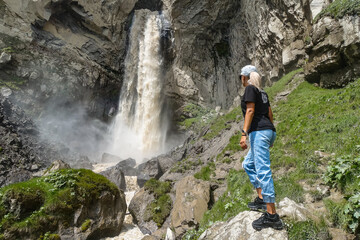 Obraz premium A girl at the Sultan-su waterfall surrounded by the Caucasus Mountains near Elbrus, Jily-su, Russia