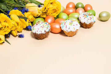 Easter cakes, eggs and yellow tulips on a beige background with space for text.