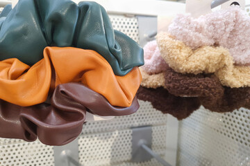 Set of trendy fluffy and leather scrunchies in shop. Brown, green, orange and beige fabric. Hair...