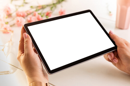 Hands holding tablet with blank screen. Spring pink flowers as background. Free copy space.