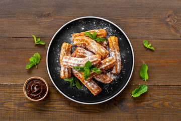 Plate with fried churros and chocolate sauce, top view