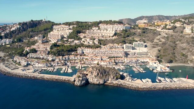Drone panning right creating a superb perspective of the costal city La Herradura. Typically Andalusian village, built on top of hill. Yacht docked, luxury real estate.