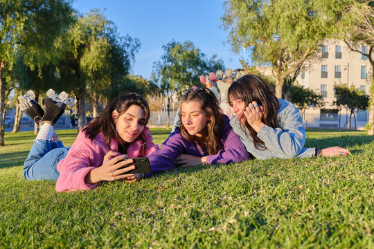 Three friends taking a selfie while lying on the grass wearing classic skates