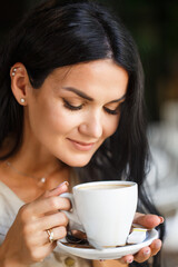 Portrait of pretty young business woman with cup in hands. Caucasian modern girl is drinking coffee in the morning in city cafe. Close up face portrait