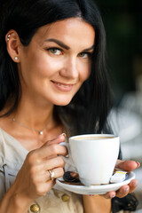 Portrait of pretty young business woman with cup in hands. Caucasian modern girl is drinking coffee in the morning in city cafe and smiling. Close up face portrait