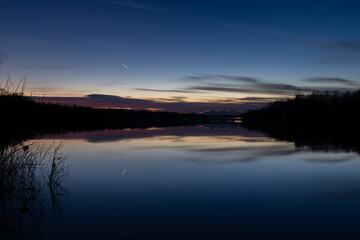 Landscape with water reflection and fading light at twilight - silhouette of forest on shore