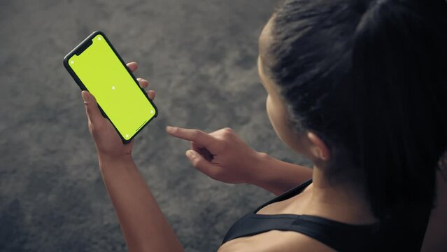 back view of fitness woman using green screen smart phone at home. Woman preparing for workout using smart phone.Woman doing a tap on mobile phone while resting during fitness training