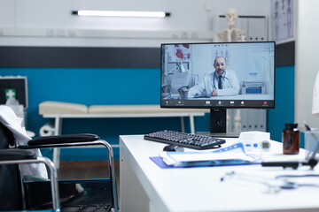 Computer screen with remote doctor discussing during online videocall meeting conference in empty hospital office room with nobody in it. Telemedicine call during clinical examination