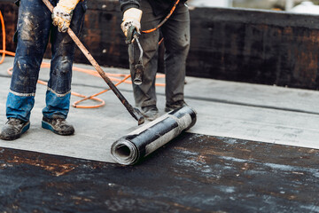 Construction workers, roofers installing rolls of bituminous waterproofing membrane.