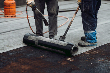Professional workers insulating rooftop with bitumen membrane and blowtorch. Waterproofing details...