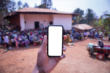 Mock up of the screen of a smartphone held by a hand with an African village in the background with...