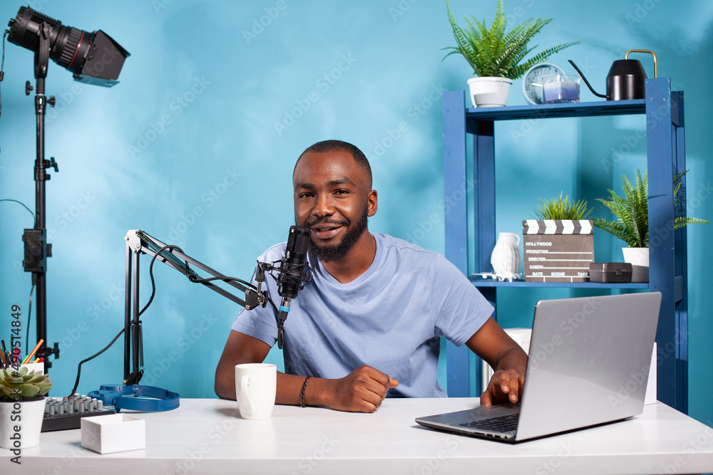 Poster smiling influencer interacting with audience during online live show looking at camera with one hand