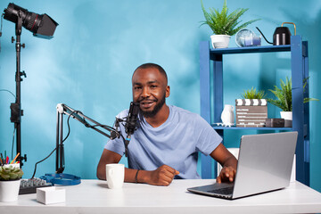 Smiling influencer interacting with audience during online live show looking at camera with one...