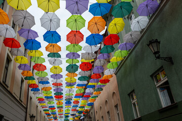 Kolorowe parasolki nad ulicą, Pszczyna. Stara kuta latarnia uliczna na budynku z zieloną elewacją.