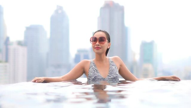 Sexy asian woman in rooftop swimming pool with modern metropolis cityscape in background