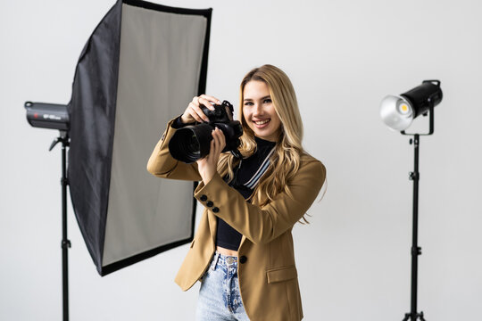 Portrait of young woman taking photos using a professional camera in the studio with lighting on the background