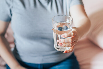 Woman sits in bed and holds glass of clean water in her hands. World Water Day. Health care concept. Drinking water in morning to boost metabolism.