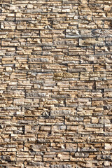 The wall is made of facing beige stone. Pattern and texture of decorative masonry.
