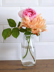 Modern kitchen, spring still life with a white brick wall. Floral composition with pink roses and orange peony in a glass vase.