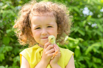 portrait of cute little girl with yellow chicken on hands on green grass outdoors. happy easter kids concept. spring child holiday