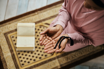 Close-up of religious Muslim woman holds prayer beads while praying in mosque.